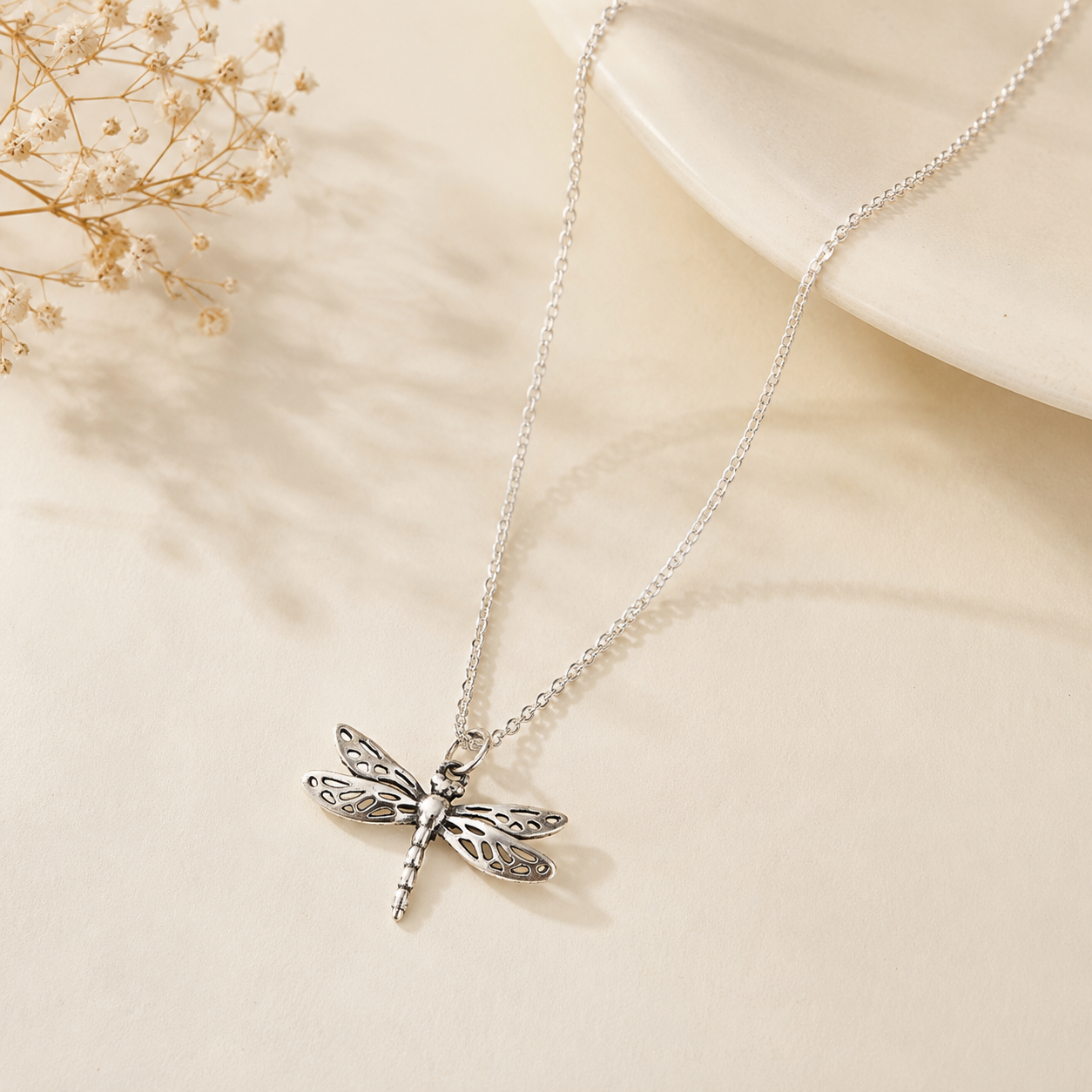 A silver dragonfly pendant necklace on a delicate silver chain, styled on a warm beige surface . Made in pure 925 sterling by silveristhan