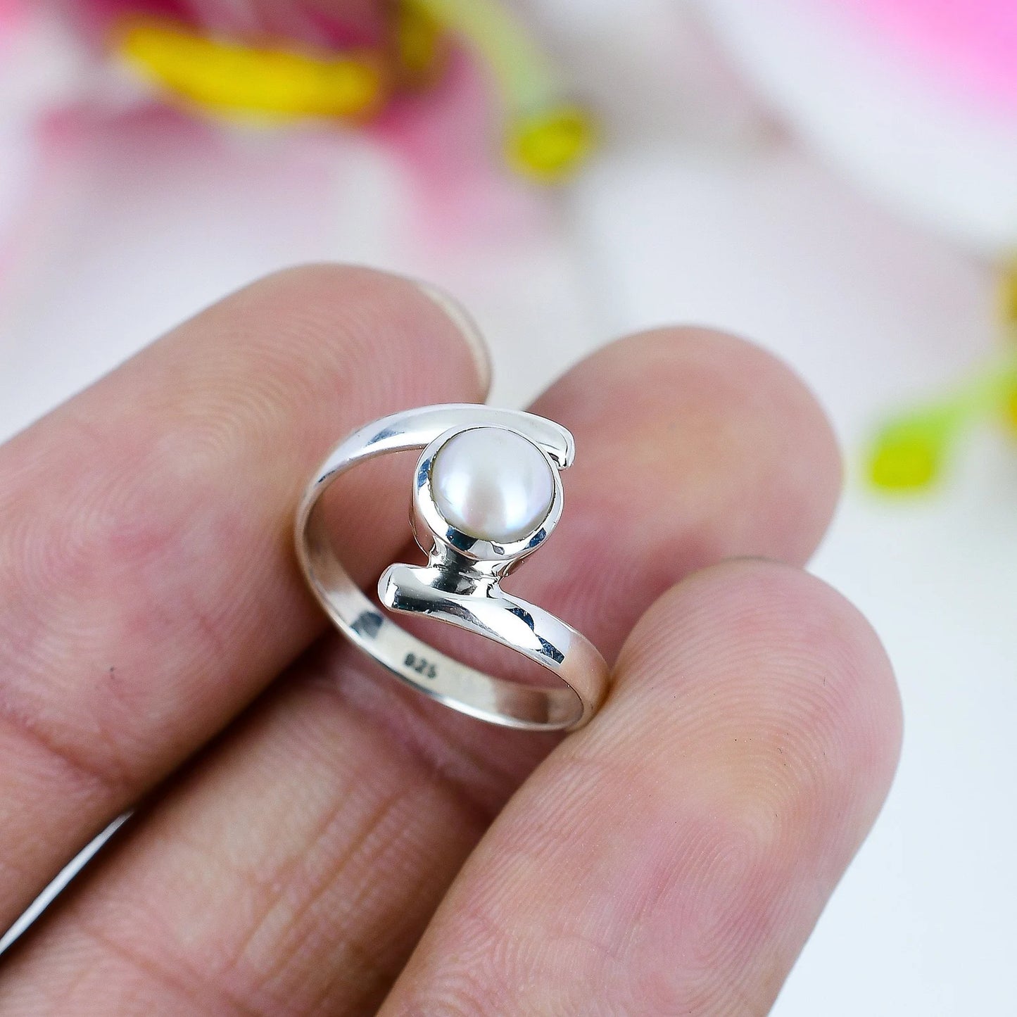A sterling silver ring with a round white pearl, held on a person's fingers against a soft, blurred background.