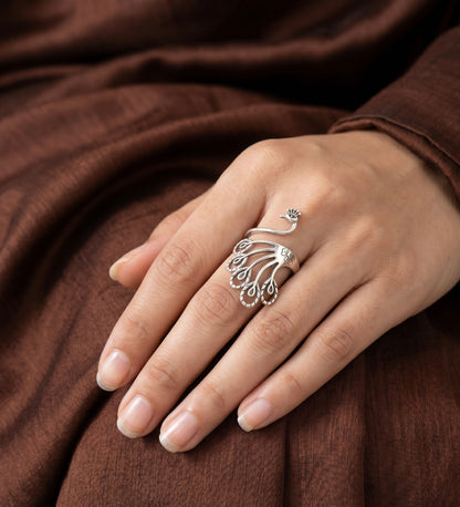 Silver peacock feather ring on a hand with a brown fabric background