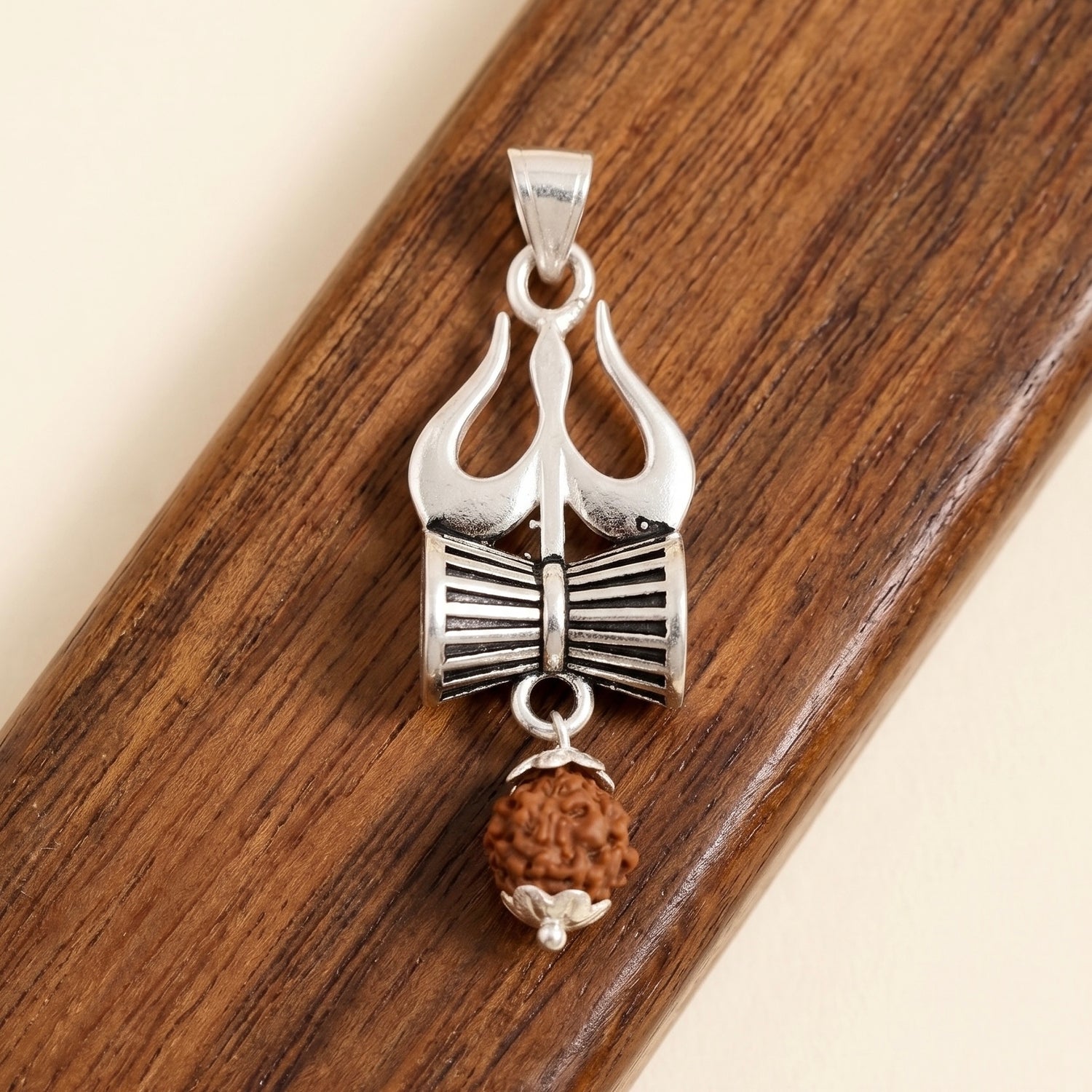 Silver Trishul and Damru Pendant with hanging panchmukhi Rudraksh on a wooden surface background.