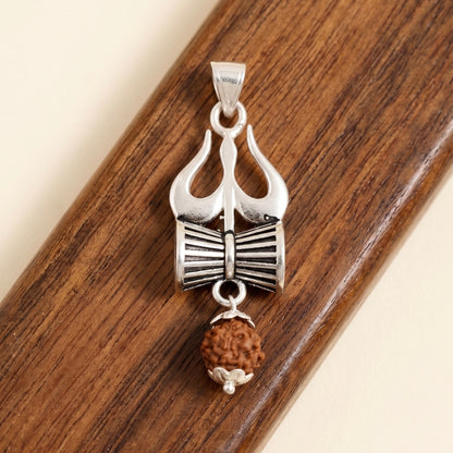 Silver Trishul and Damru Pendant with hanging panchmukhi Rudraksh on a wooden surface background.