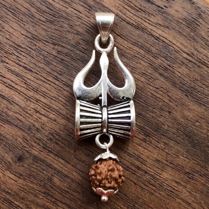 Close Up image of Silver Trishul Damru pendant with hanging panchmukhi rudraksh on a dark wooden surface by silveristhan
