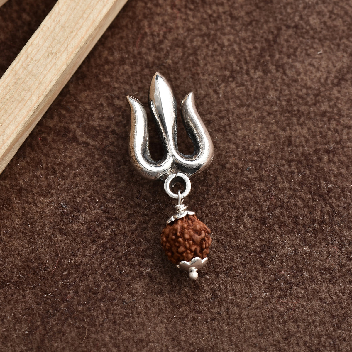 A trishul shaped brooch made in pure silver kept on grainy brown surface. 