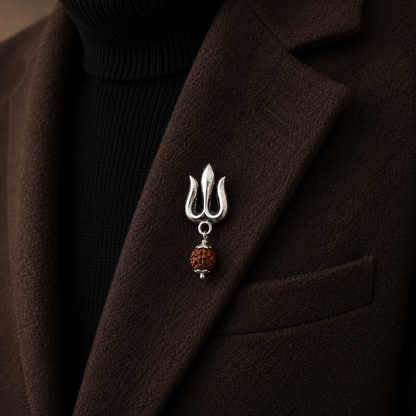 A sterling silver made brooch shaped like a trident with hanging rudraksh, pinned to the lapel of a dark brown coat over a black ribbed turtleneck.